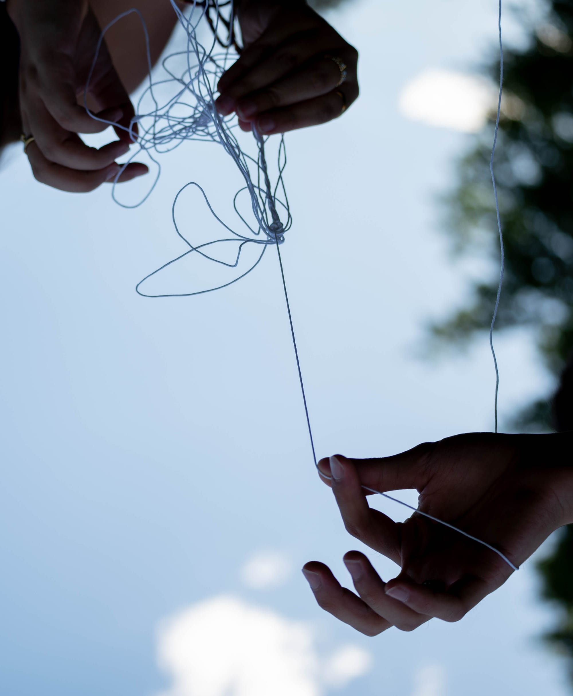 Photos of three hands untangling string set against a blue sky, taken upside-down